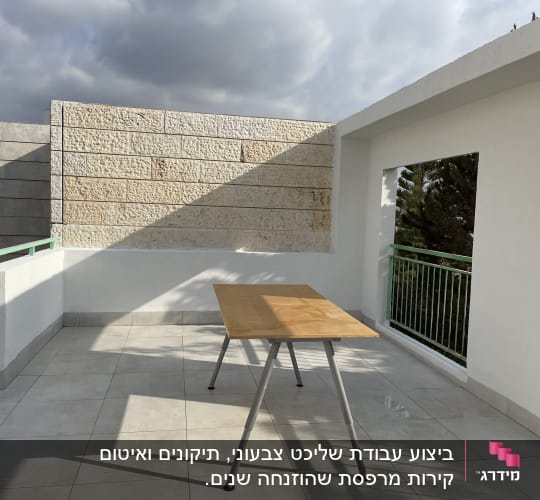 מרפסת עם שולחן עץ ורקע של קיר אבן